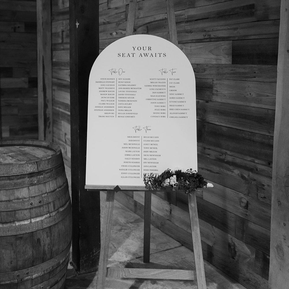Seating chart on a stand against a wooden wall with a barrel in the background