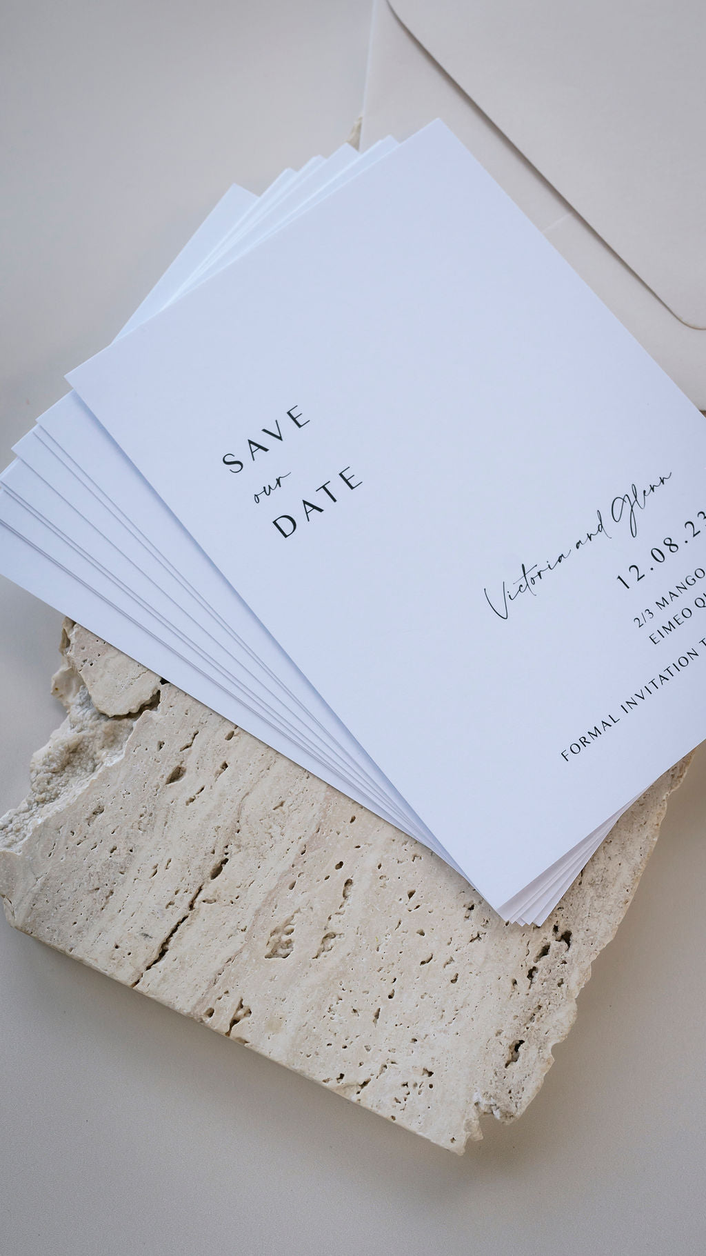 Save the date lettering on an invitation in a brown kraft envelope, shot from above on a pink pastel background with a rose