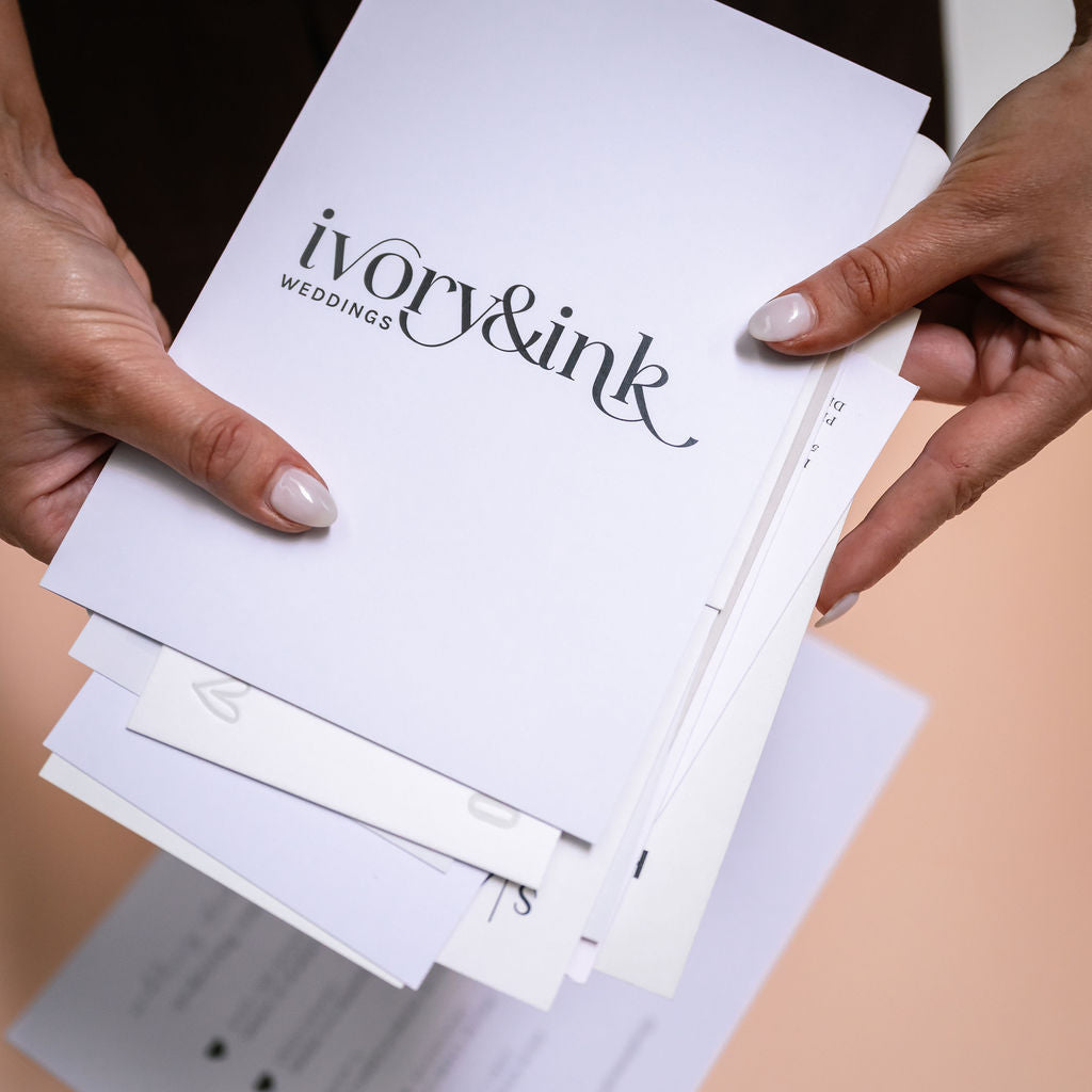 Hands holding a stack of Ivory & Ink wedding invitations, showing a range of design styles