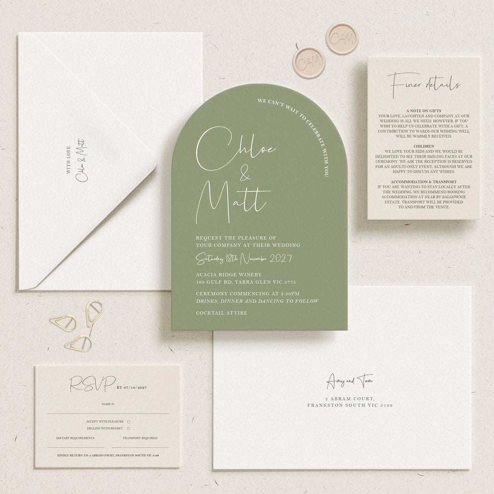 A styled flat-lay of a wedding invitation suite on a light textured background, featuring a sage green arch-shaped invitation card, white envelopes, a details card, a RSVP card, and small gold foil accents.