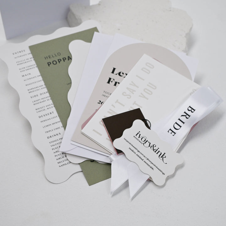 Wedding stationery samples including a wavy edge menu, invitation, card stock swatch, place tag and bride ribbon