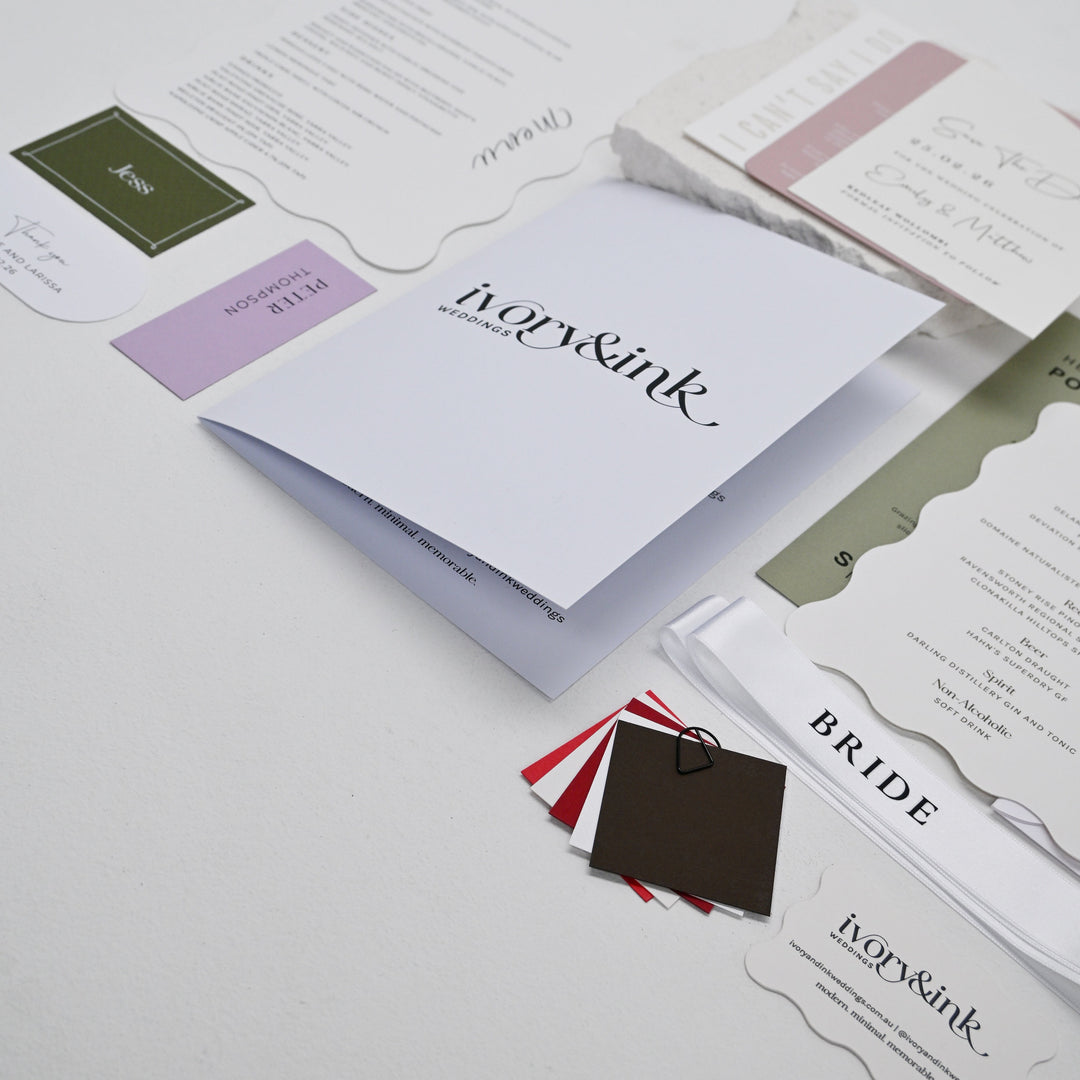 Contents of the Ivory &amp; Ink wedding stationery sample pack laid out, including invitations, menus, card stock swatches and a bride ribbon
