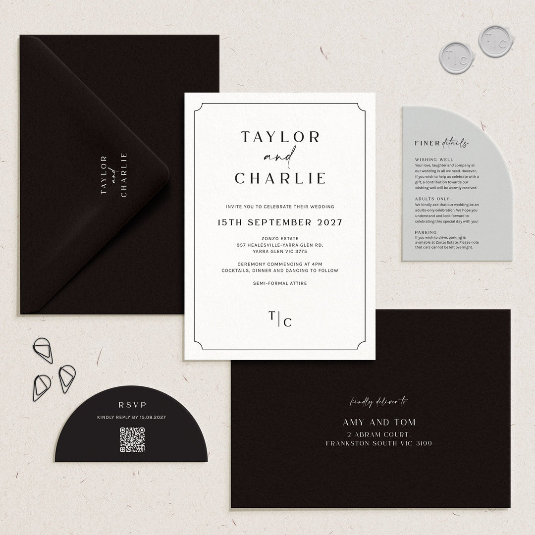 A styled flat-lay of a wedding invitation suite on a light textured background, featuring a white main invitation card, black envelopes, a gray details card, and a black RSVP card with small decorative metal accents.